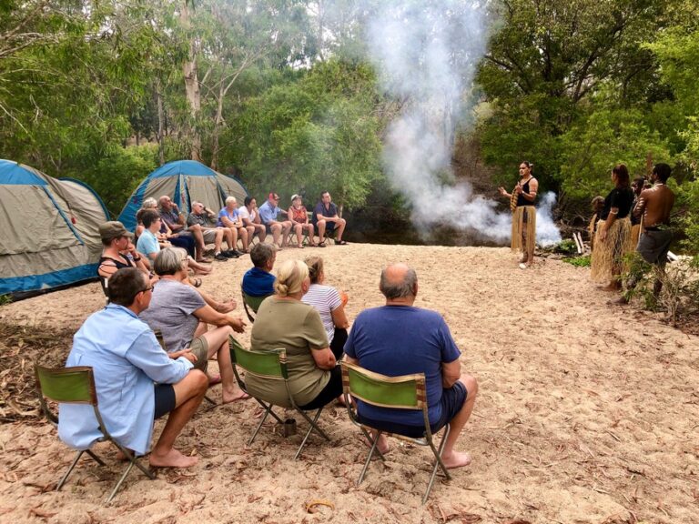 group of people sitting around fire receiving welcome to country by aboriginal lady